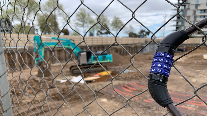 A closed construction site, seen through a chain link fence with a bike lock hanging off it