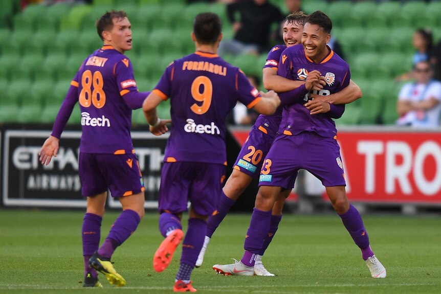 Dane Ingham is hugged by his teammate as two other people in purple kit run towards him