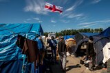 Migrants walk past a flag of England inside the "Jungle" camp for migrants and refugees in Calais on June 24, 2016