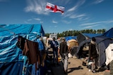 Migrants walk past a flag of England inside the "Jungle" camp for migrants and refugees in Calais on June 24, 2016
