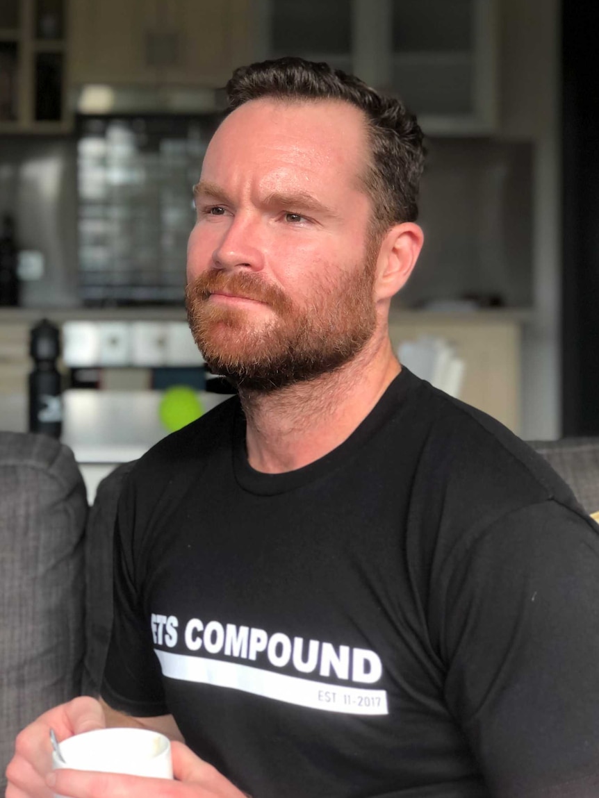 A man wearing a black t-shirt sits on a couch