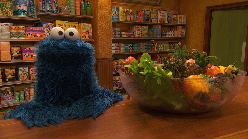 Cookie Monster standing next to a bowl of fruit and vegetables