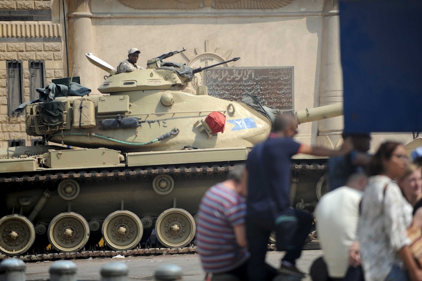 A soldier inside a tank stands guard outside Tora prison while journalists wait to enter a court in Cairo