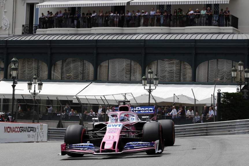 Sergio Perez drives in a white car with fans watching on from a building behind him