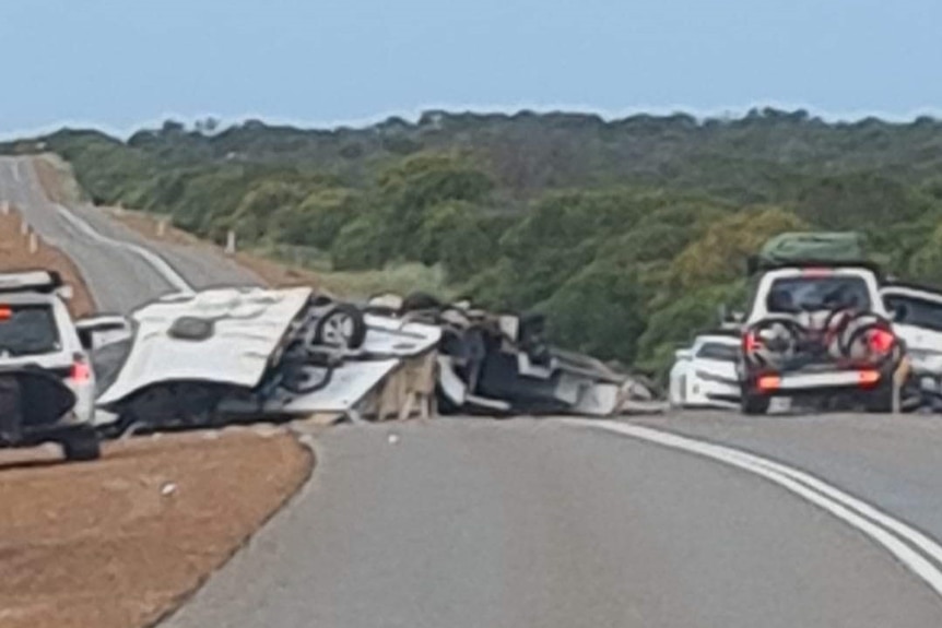 A destroyed caravan on a rural highway, with other vehicles around it.