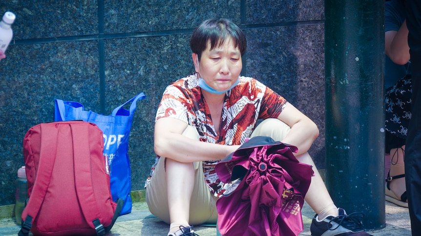 Chinese woman sitting on the floor outside a building, crying 