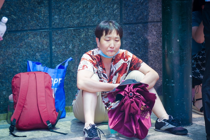 A Chinese woman sitting on the floor outside a building, crying 