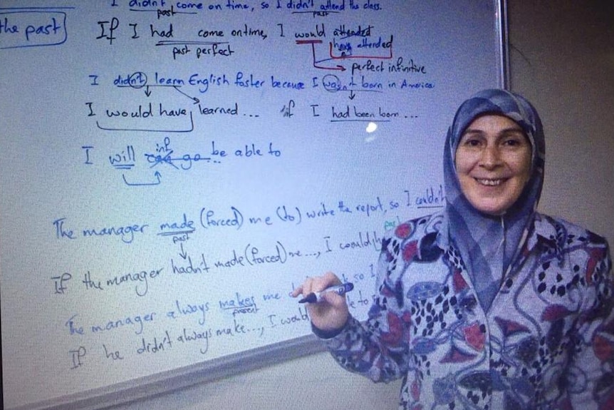 Amina stands in front of a white board her language school in Aleppo