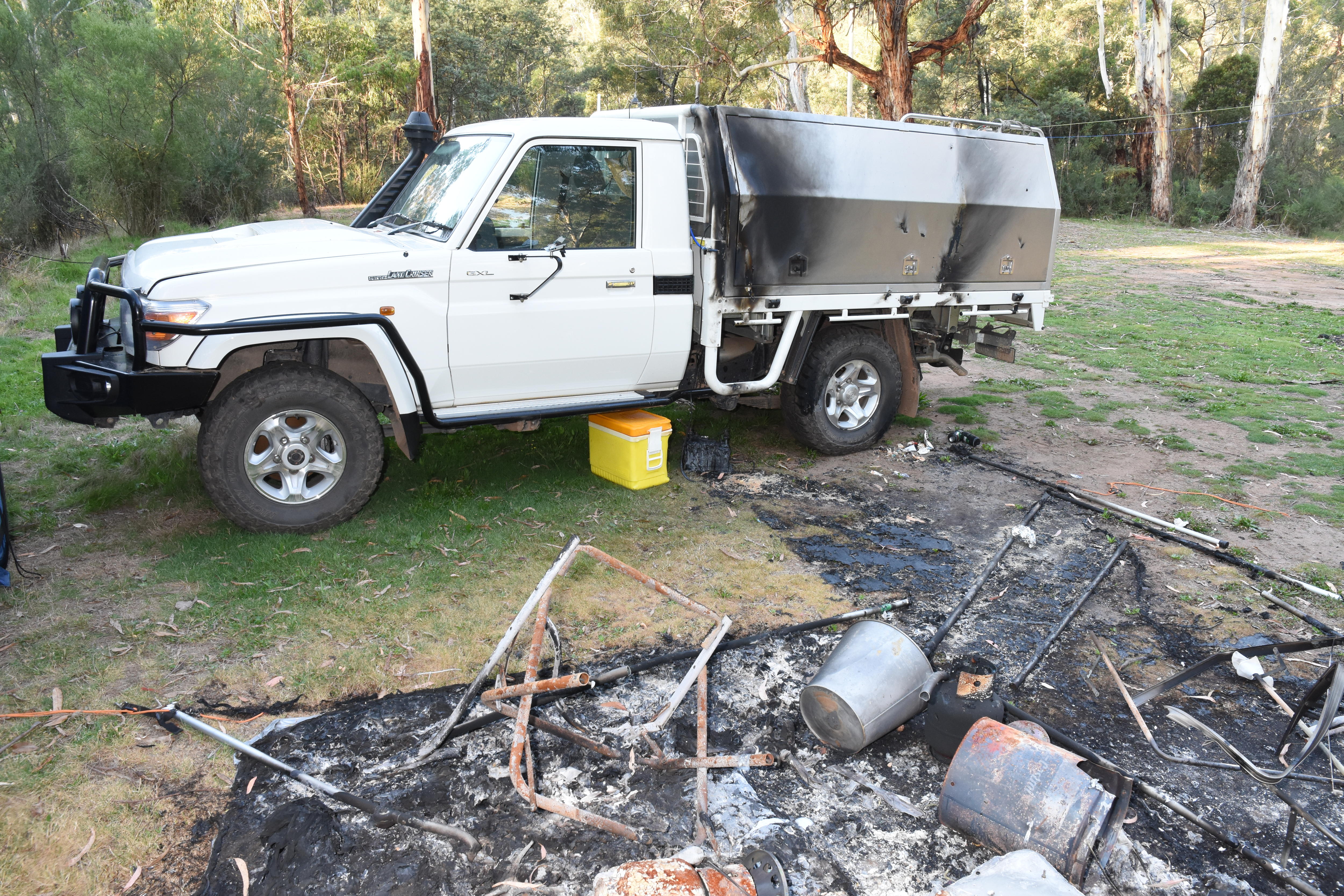 A photo of a white Landcruiser with a charred campsite beside it.