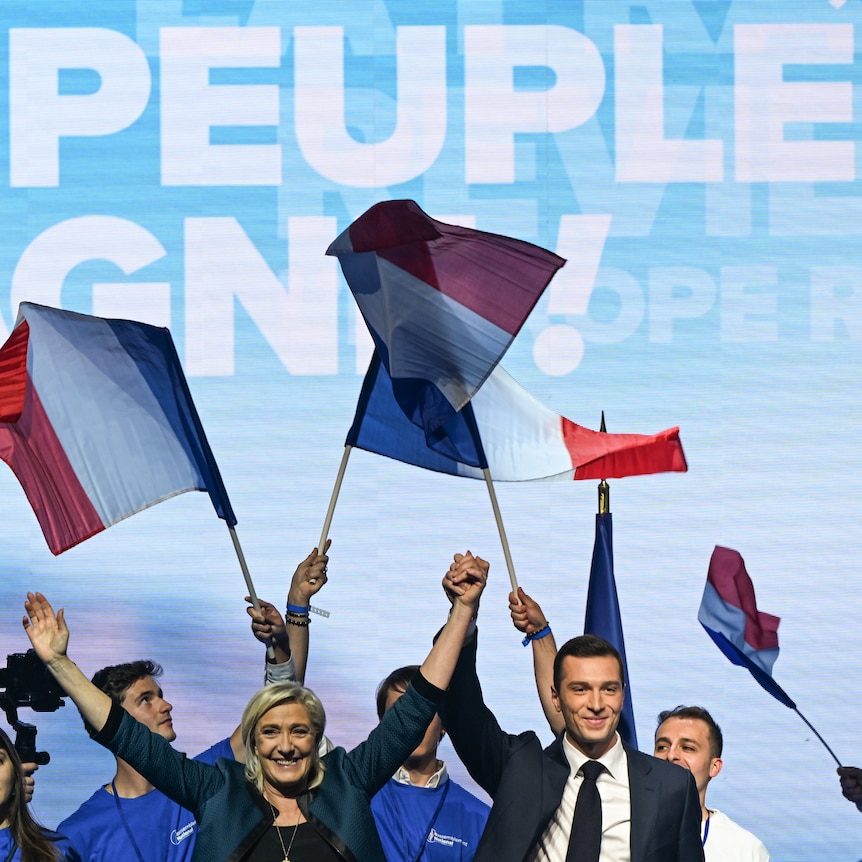 Marine Le Pen and Jordan Bardella celebrate on stage amongst supporters and French flags. 