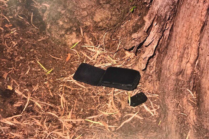 A police image of a black wallet and single car key placed by a tree.