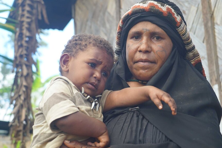 PNG widow Bessie Peyabe dressed in black mourning robes holds her young son