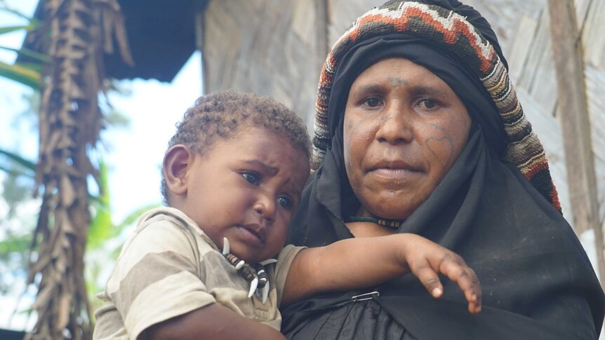 PNG widow Bessie Peyabe dressed in black mourning robes holds her young son