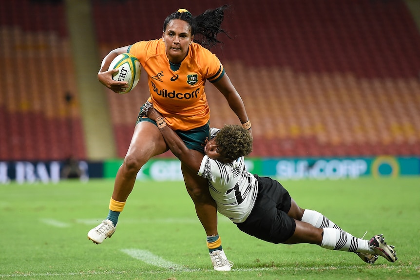 A Wallaroos player holds the ball as a Fijina opponent attempts to make a tackle.
