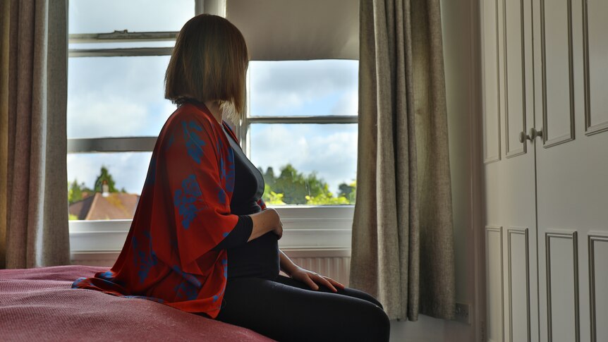 Lone pregnant woman sitting on the bed looking out at the window in the morning.