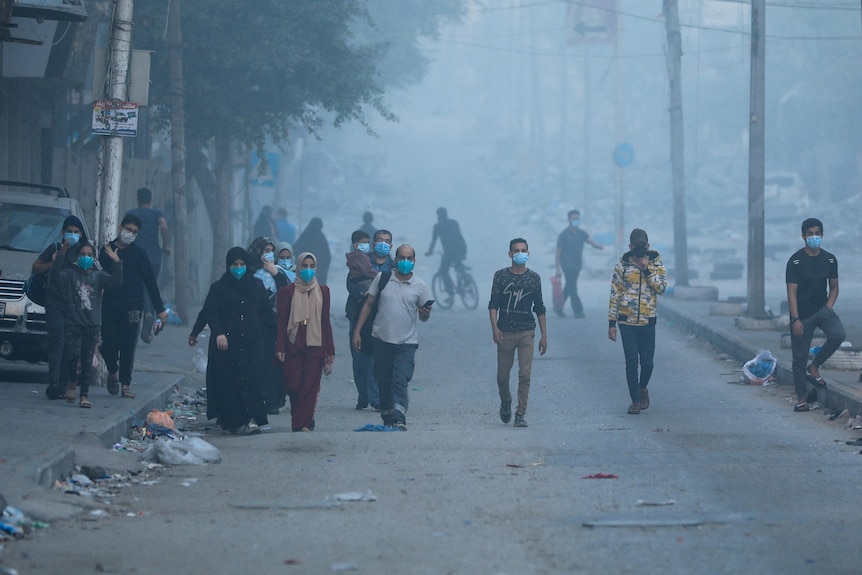 A group of people wearing masks walking through a dirty street that is filled with white dust