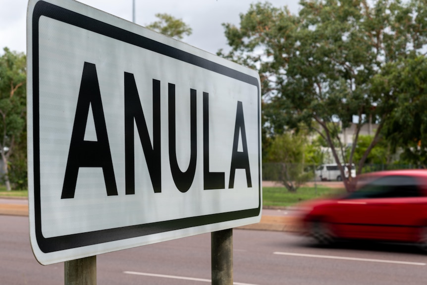 A street sign reading Anula, a car drives past in the background.