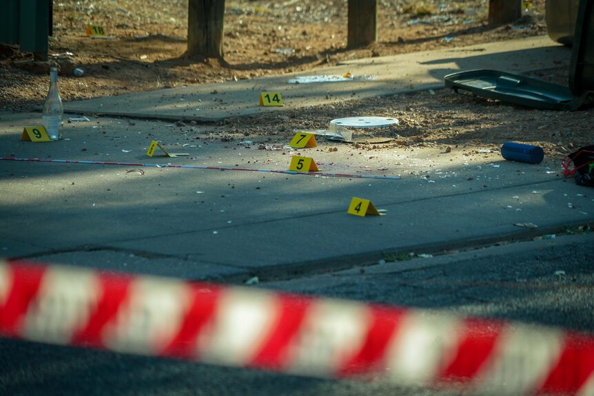 Red-and-white police tape around a street with broken glass everywhere.