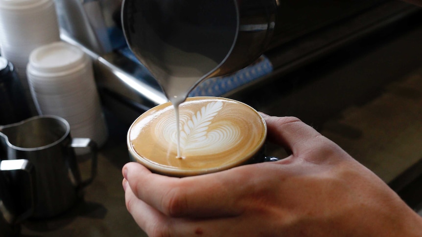 Hand of barista pouring a latte coffee with pattern