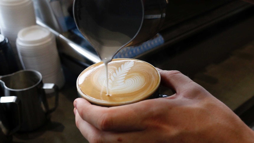 Hand of barista pouring a latte coffee with pattern.