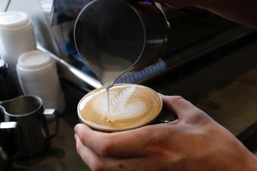 Mano de barista sirviendo un café con leche con patrón.