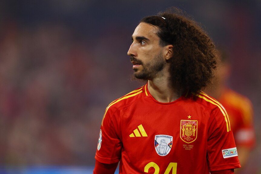 Marc Cucurella looks to his right as he stands on a stadium pitch. 