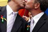 Two men in suits kiss.