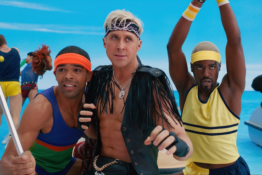 A Black man in blue and green sportswear, a white man in a black leather vest and a Black man in yellow sportswear stand braced