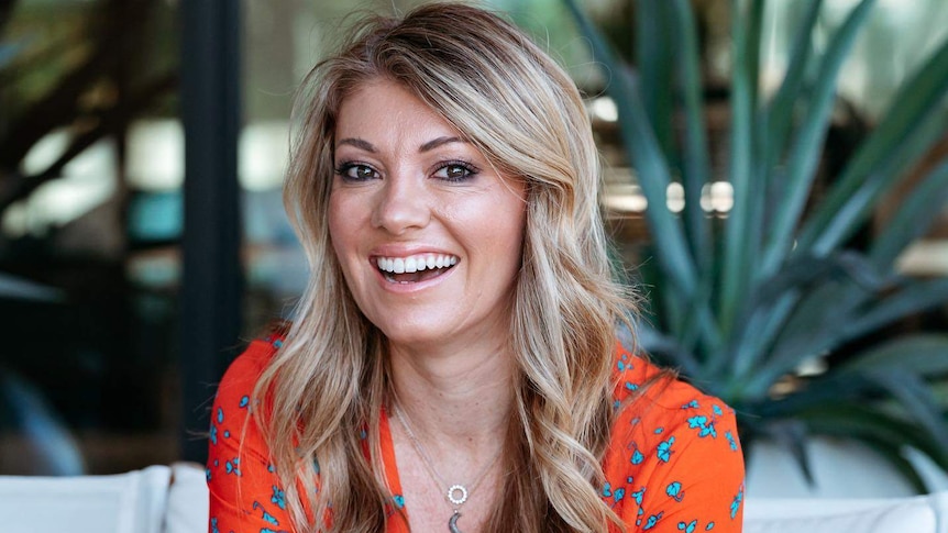 Natalie Kringoudis wearing a bright orange dress and smiling.