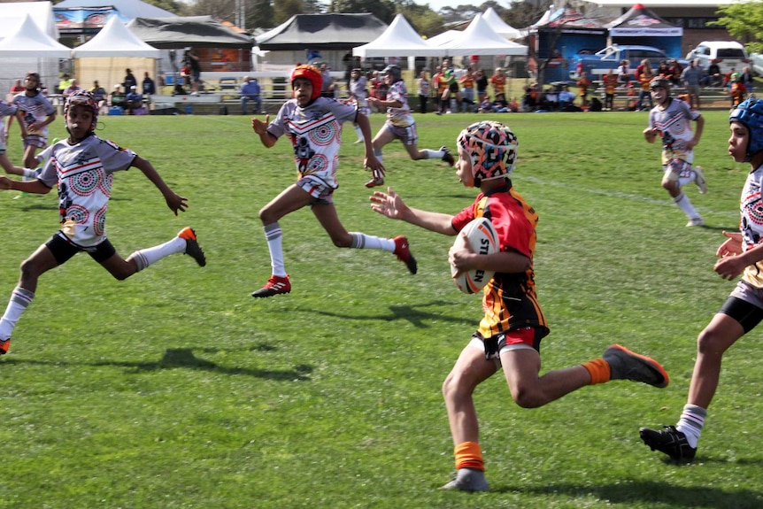 Young Indigenous rugby players running on the field.