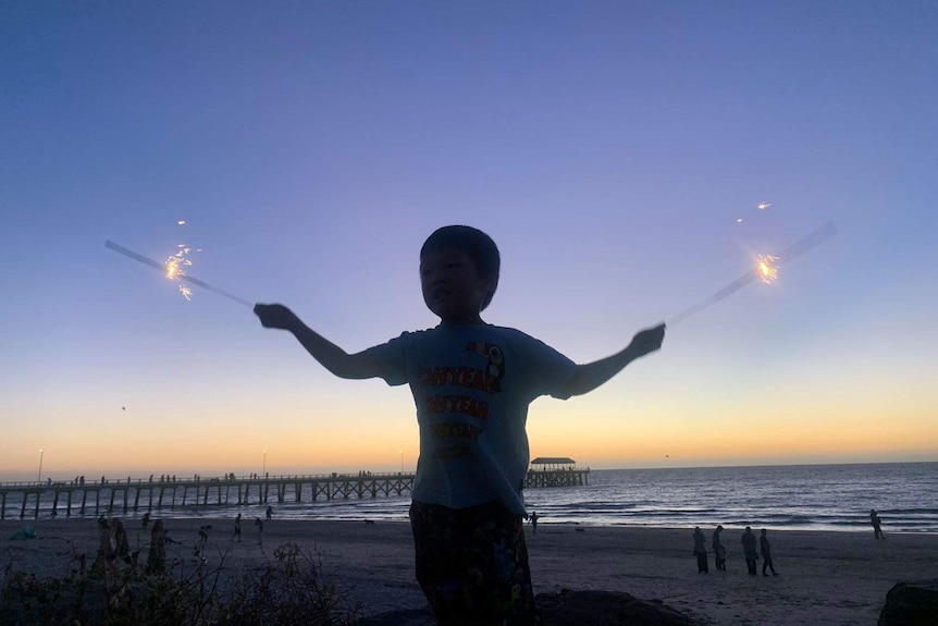 A young boy holds sparklers at sunset on Henley Beach in Adelaide.