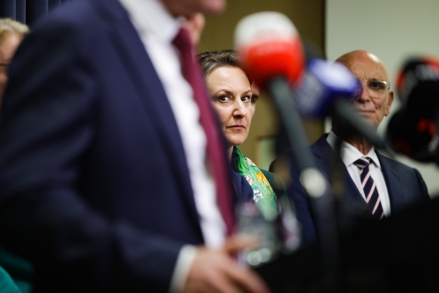 Amber-Jade Sanderson looks to her left sandwiched between John Quigley and an unseen Mark McGowan at a media conference.