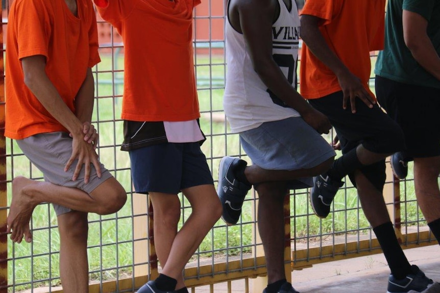 Boys lean against fence at youth detention centre.