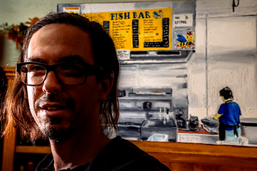 A close up of a man with a painting of a woman working in a fish shop behind him.