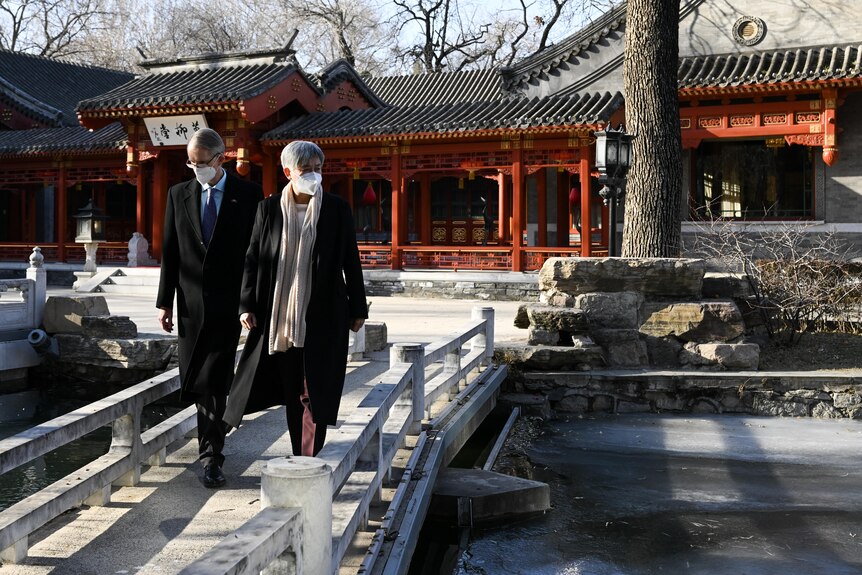 Penny Wong and Graham Fletcher walk across a bridge in front of an ornate Chinese style house. 