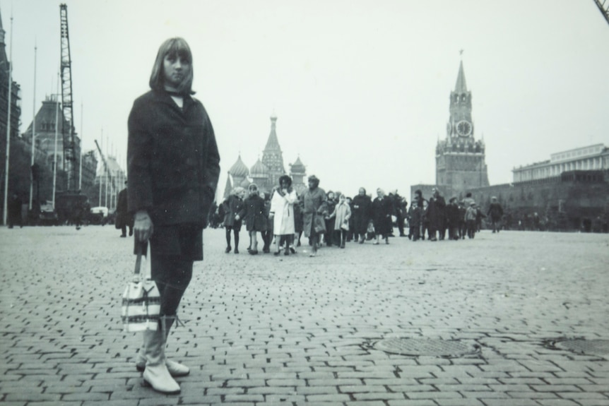 Black and white photo of young girl with shoulder-length, with one hand in pocket and the other holding a handbag.