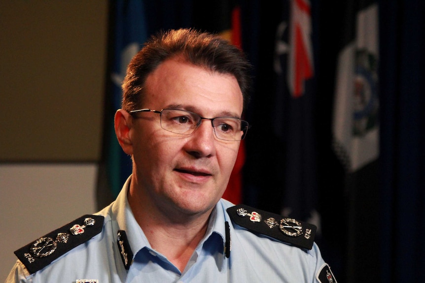 La commissaire de l'AFP, Reece Kershaw, en uniforme avec des drapeaux accrochés derrière lui dans une pièce, prend la parole lors d'un entretien.