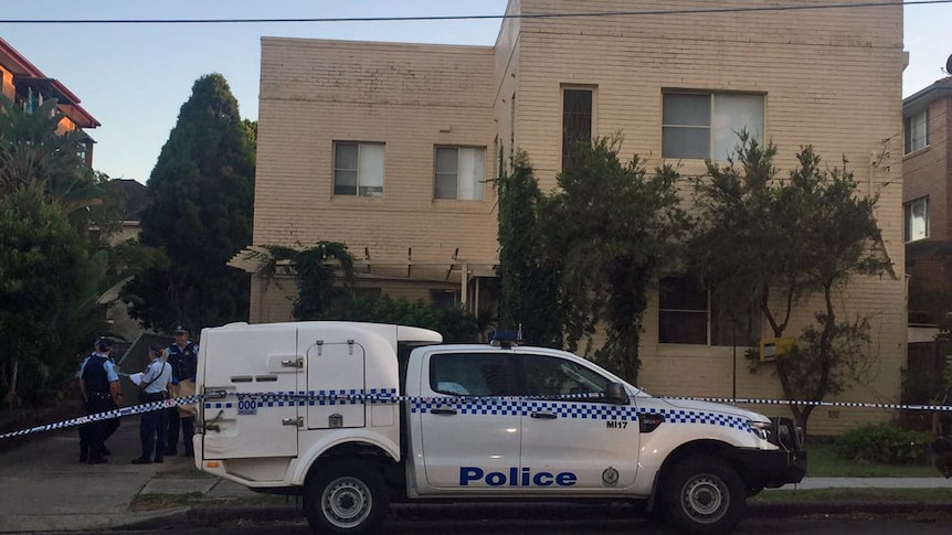 Several police officers gather outside a home at Cronulla, which is surrounded by police tape.