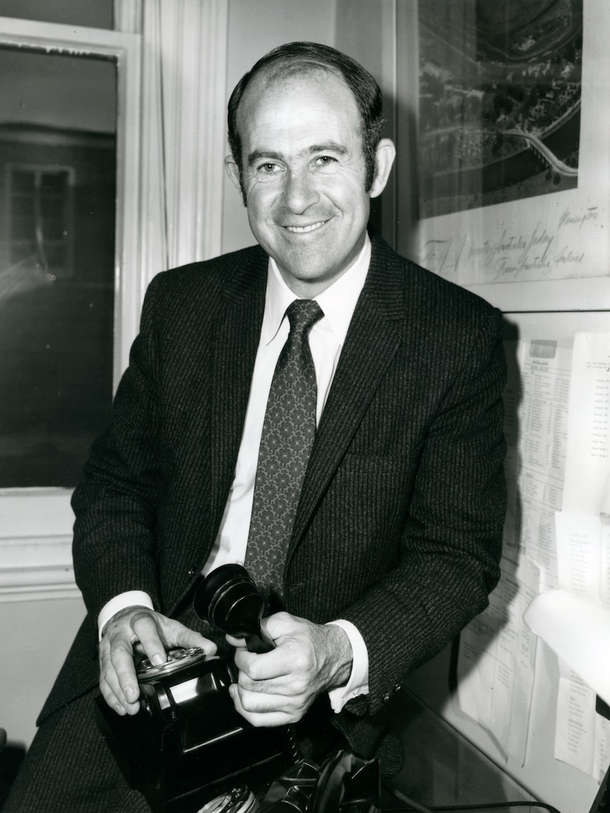 Black and white photo of man holding an old fashioned telephone.