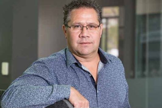 Shane Mohor leaning on a ledge wearing glasses and a button-up shirt