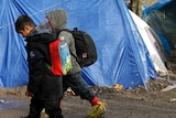 Two children walk past a tent at a muddy asylum seeker camp in northern France.