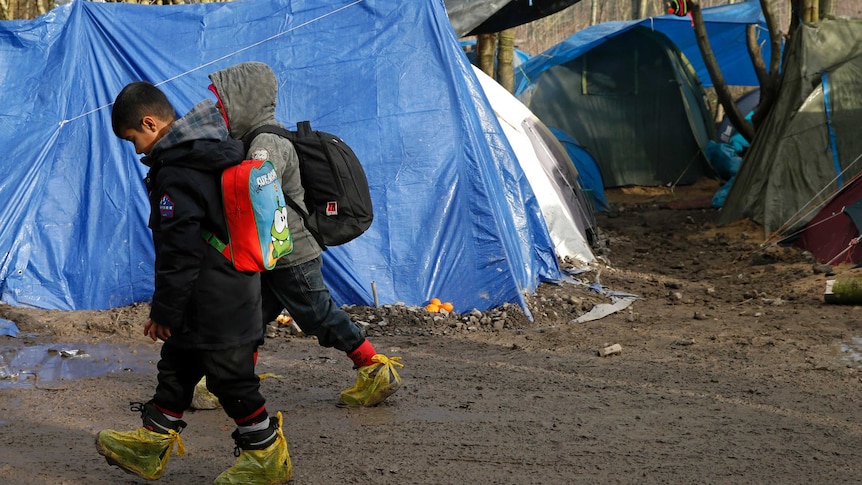 Two children walk past a tent at a muddy asylum seeker camp in northern France.