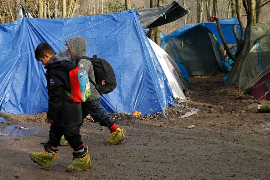 Two children walk past a tent at a muddy asylum seeker camp in northern France.