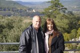Former police officer Bruce Cooper, with wife Michelle Schlitter, smiling, with a view of mountains and trees in background.