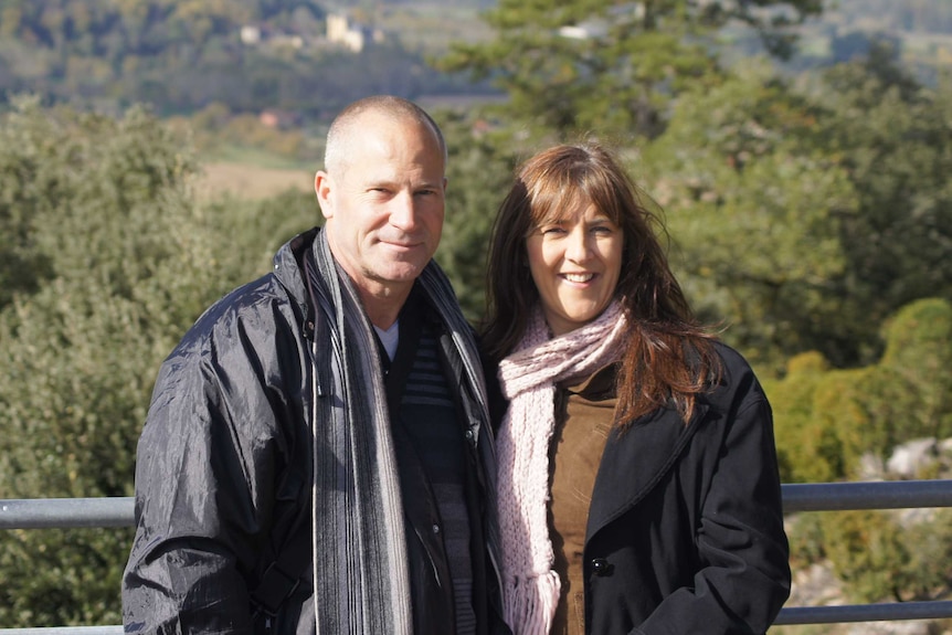 Former police officer Bruce Cooper, with wife Michelle Schlitter, smiling, with a view of mountains and trees in background.