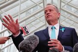 Bill Shorten gestures to microphones he is wearing a suit with a pale blue tie.