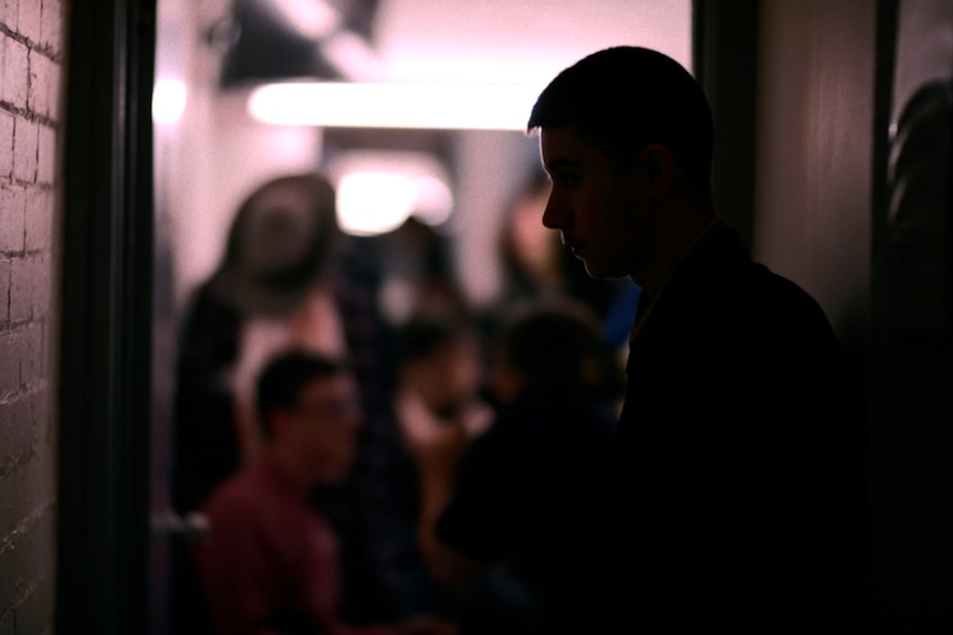 A silhouette of a student in a corridor backstage at a theatre. The room in the background is out of focus.