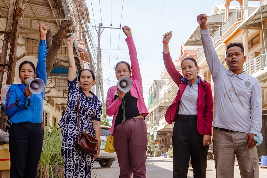 Four women and a man raise their fists in the air, with some holding megaphones.