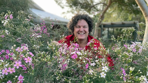 Jossh Byrne standing behind a flowering shrub.