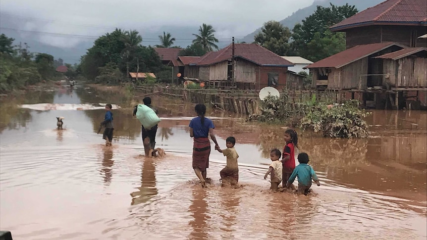 Seven people, five of them children, wade through a village street flooded with muddy water